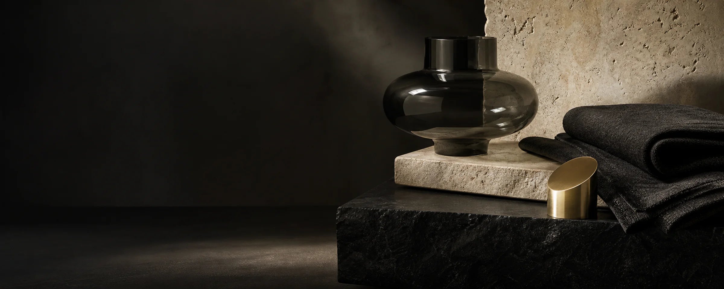 Smoked glass, limestone, brushed metal, and charcoal textile in a dark gallery setting